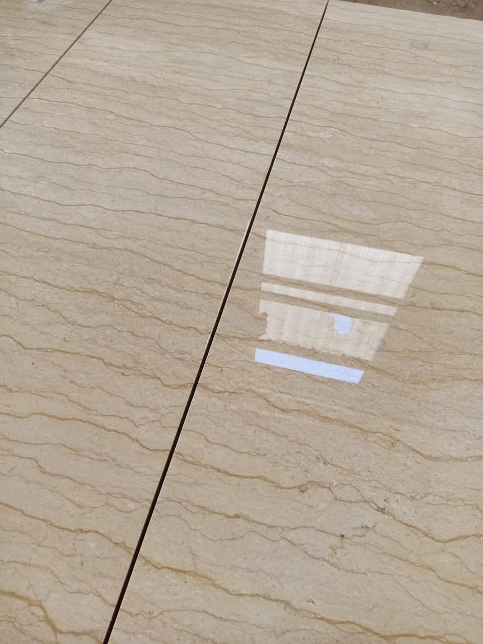 Close-up of polished beige marble tiles with subtle veining patterns and reflections from a window.