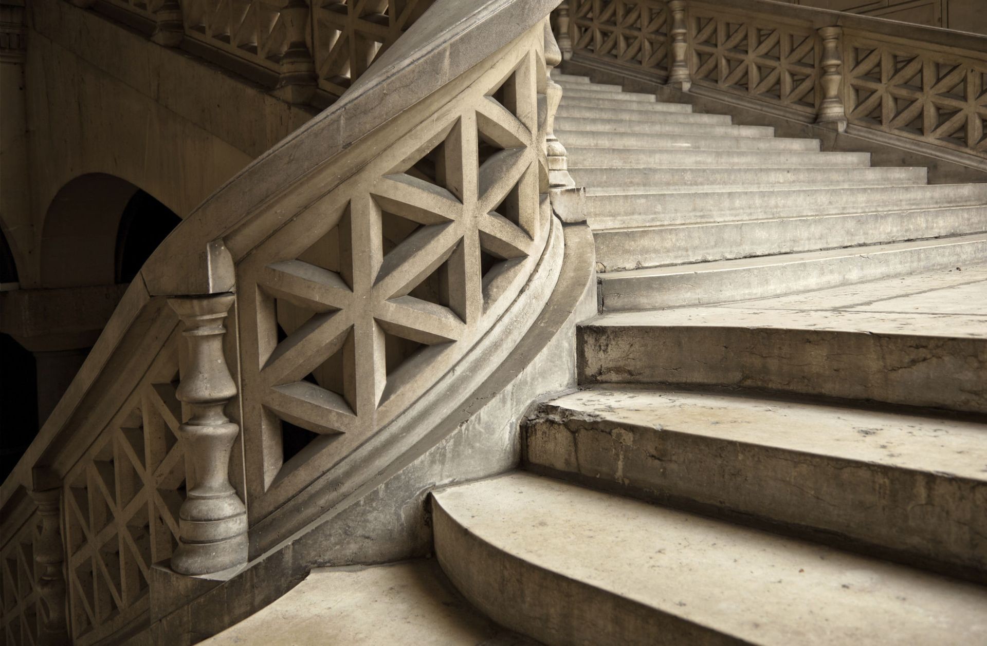 Elegant stone staircase with intricate geometric railing design in a historic building.